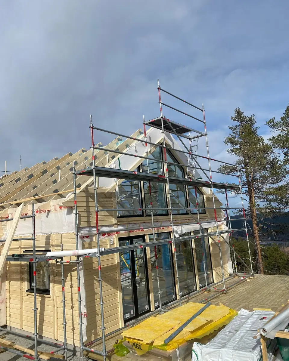 Trähus under byggnation med stora glaspartier i gaveln.