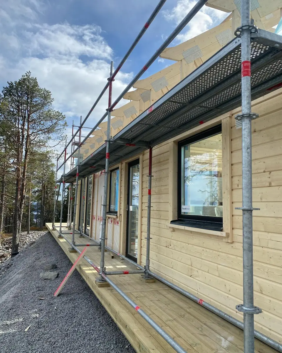 Närbild av träfasad, fönster och byggställning på ett nytt hus.