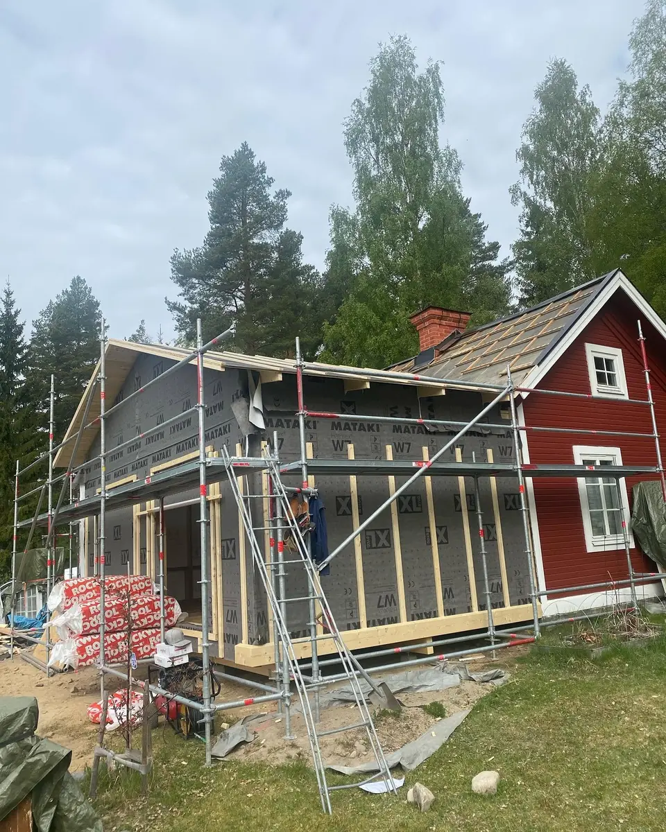 Bred tillbyggnad på rött hus under arbete med byggställning.