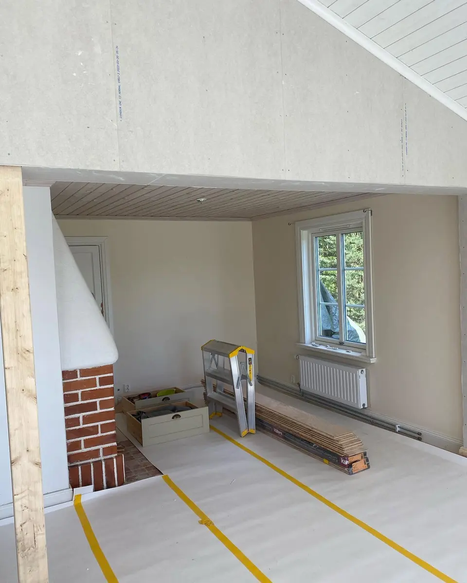 Rum under renovering med öppen spis och skivklädda väggar.