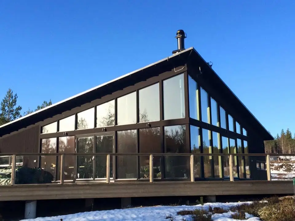 Färdig mörk träbyggnad med stora glaspartier och altan.