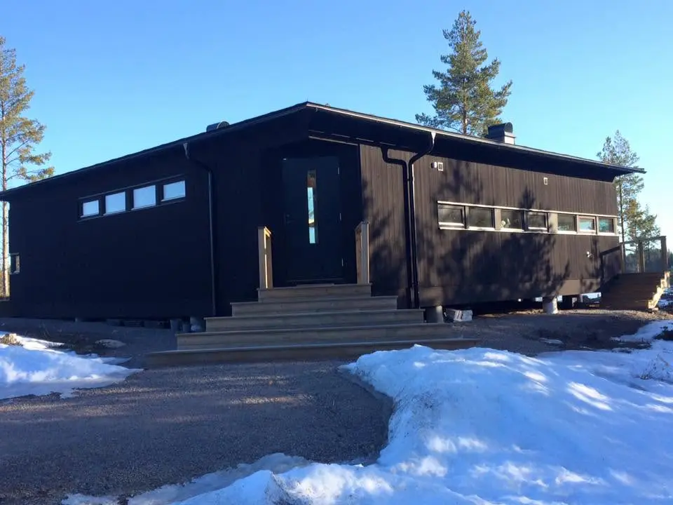Entrésida på mörk träbyggnad i vintermiljö.