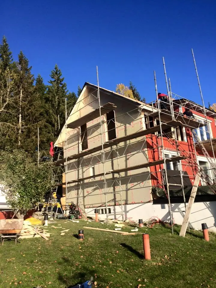 Tillbyggnad på rött hus med isolerad fasad och byggställning.