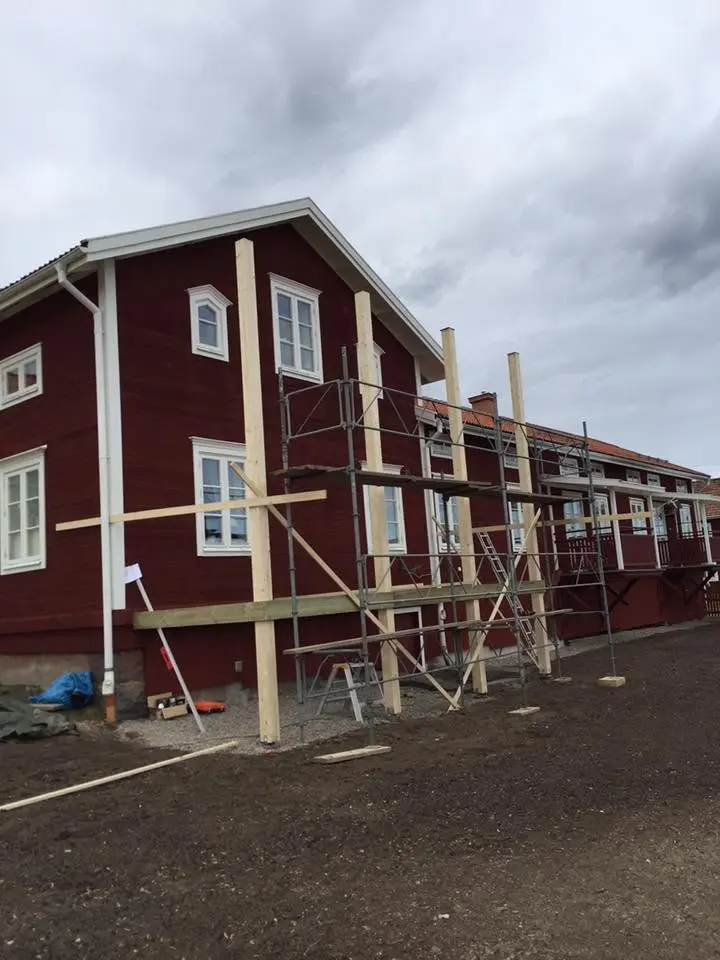 Ny träkonstruktion längs fasaden på ett äldre rött trähus.