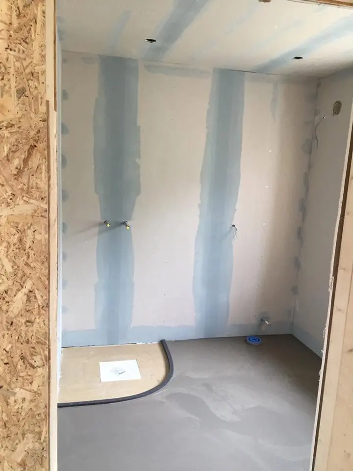 Mindre rum under renovering med monterade gipsskivor och förberedda rör.