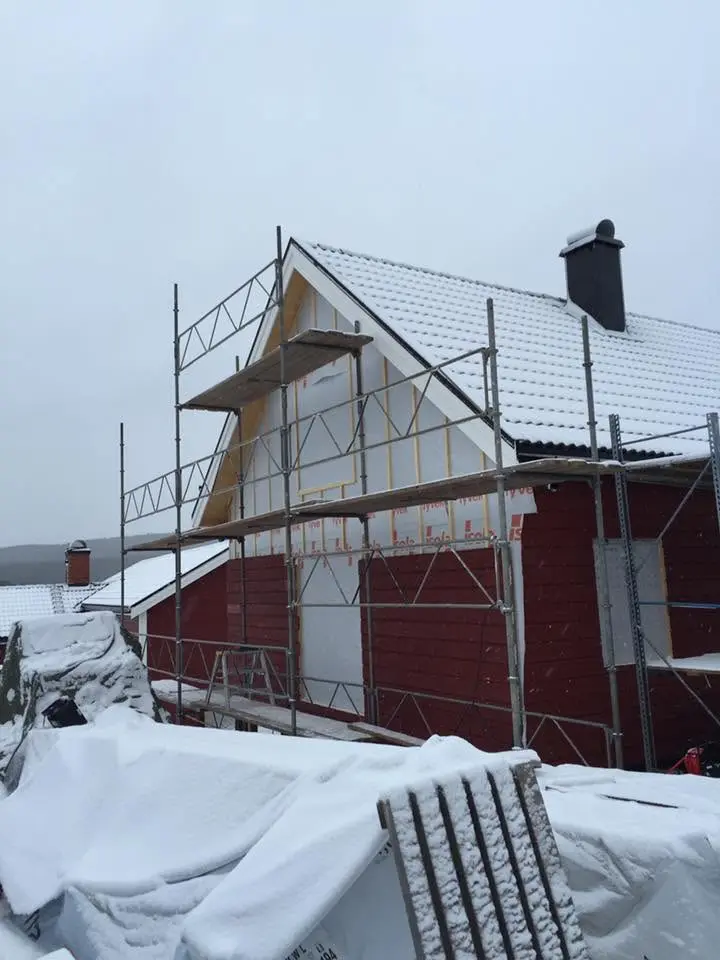 Tillbyggnad på rött hus under arbete i snö med byggställning.